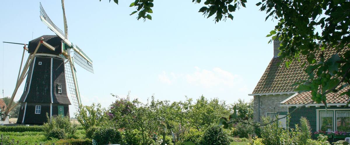 A traditional windmill, a stone house, and lush greenery.