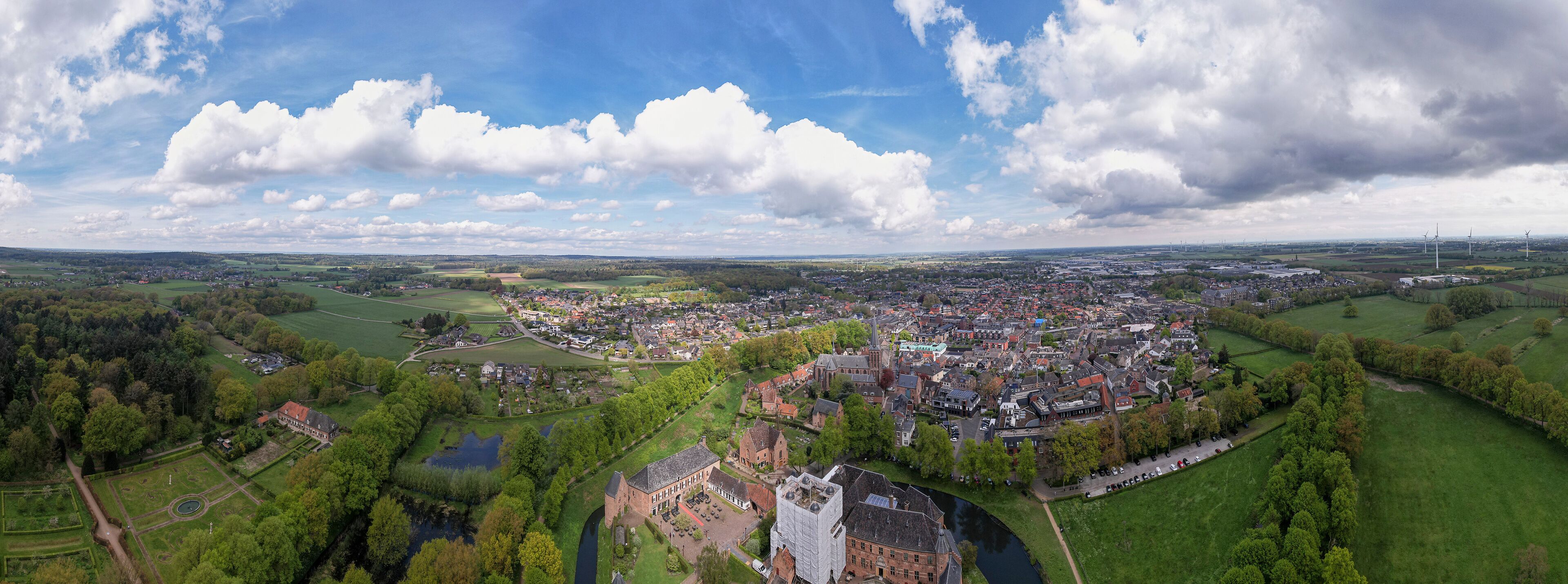 An aerial view of a town with a river, green fields, and wind turbines in the distance.