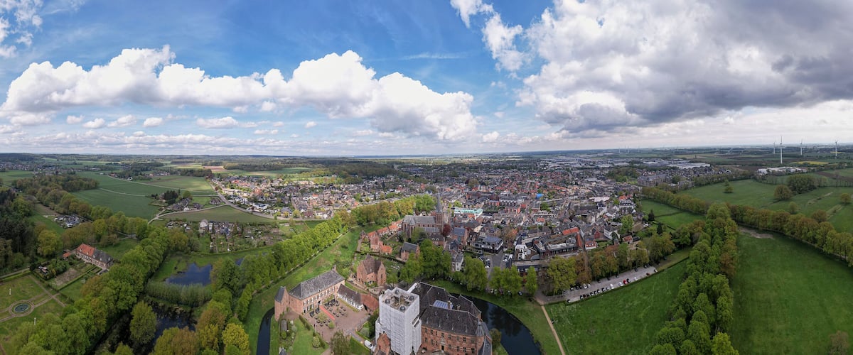 An aerial view of a town with a river, green fields, and wind turbines in the distance.