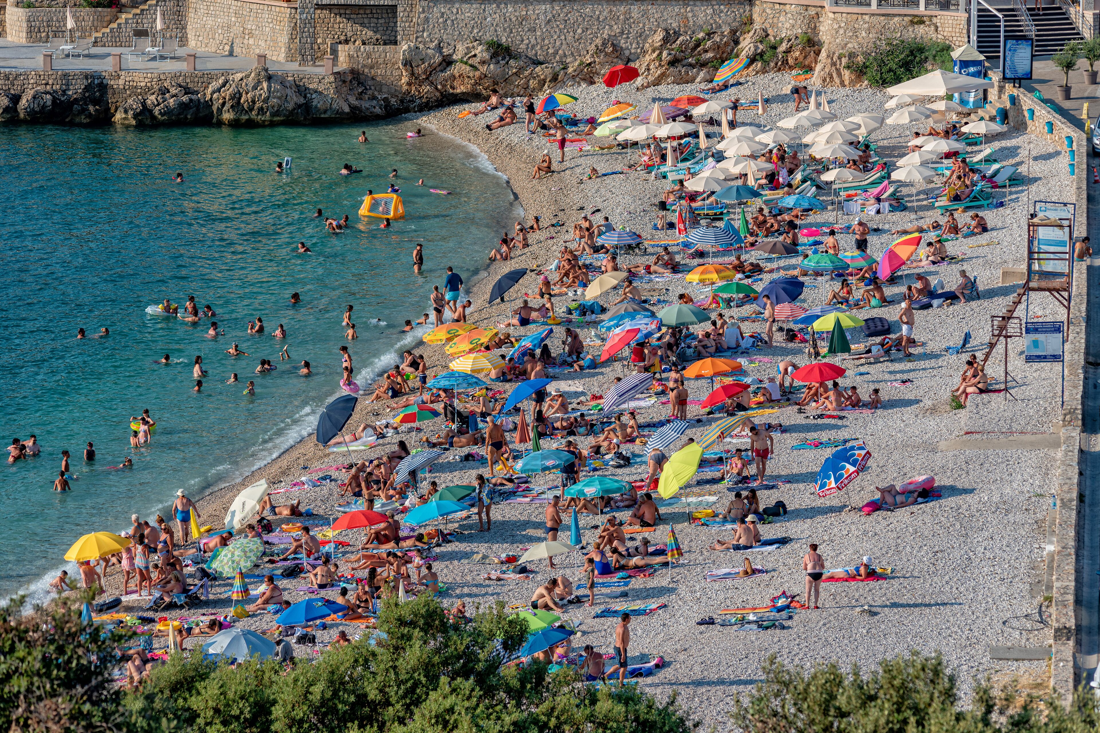 A crowded beach with people sunbathing and swimming, surrounded by colorful umbrellas.