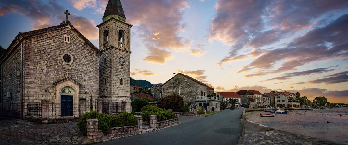 A stone church with a bell tower and a clock, set against a sunset sky.
