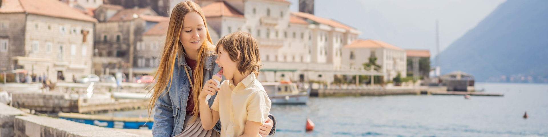 Mom and son tourists enjoying Colorful street in Old town of Perast on a sunny day, Montenegro. Travel to Montenegro concept. Scenic panorama view of the historic town of Perast at famous Bay of Kotor