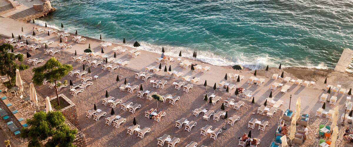 A beach with rows of sun loungers and umbrellas, a stone walkway, and the ocean.