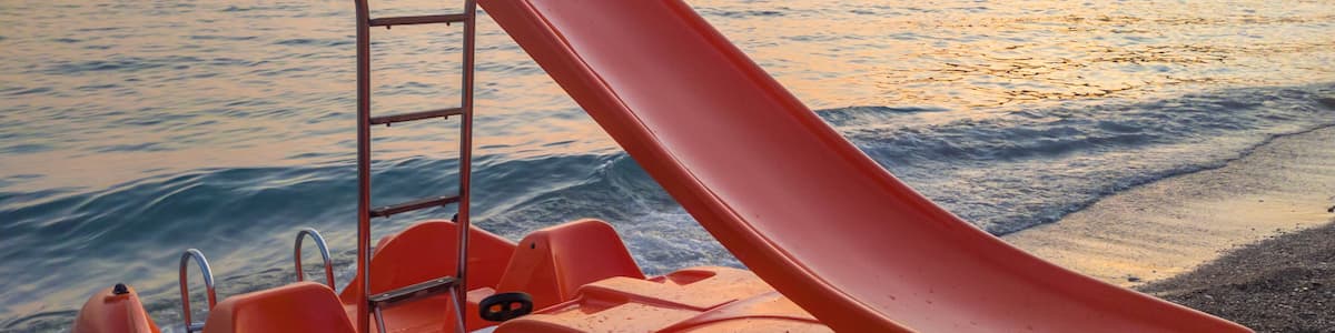 Slide on orange pedal (paddle) boat - pedalo parked on a sandy beach at sunset. Calm blue sea water and clear pink sky in the background. In Canj (Čanj) Montenegro.