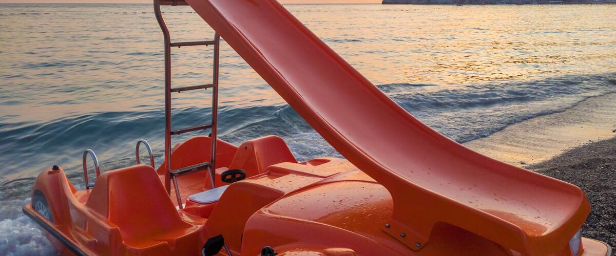 A red water slide on a beach with waves and a sunset in the background.