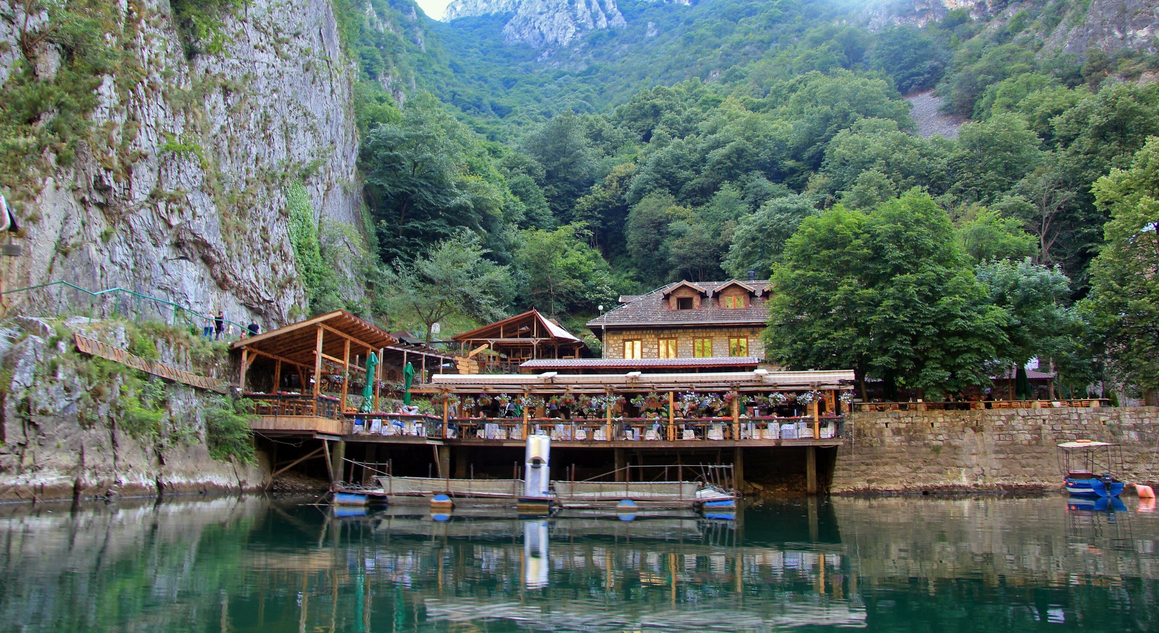 A wooden bridge over a river with buildings and trees in the background.