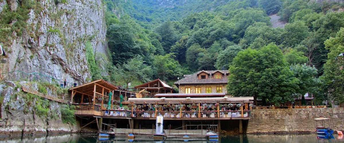 A wooden bridge over a river with buildings and trees in the background.