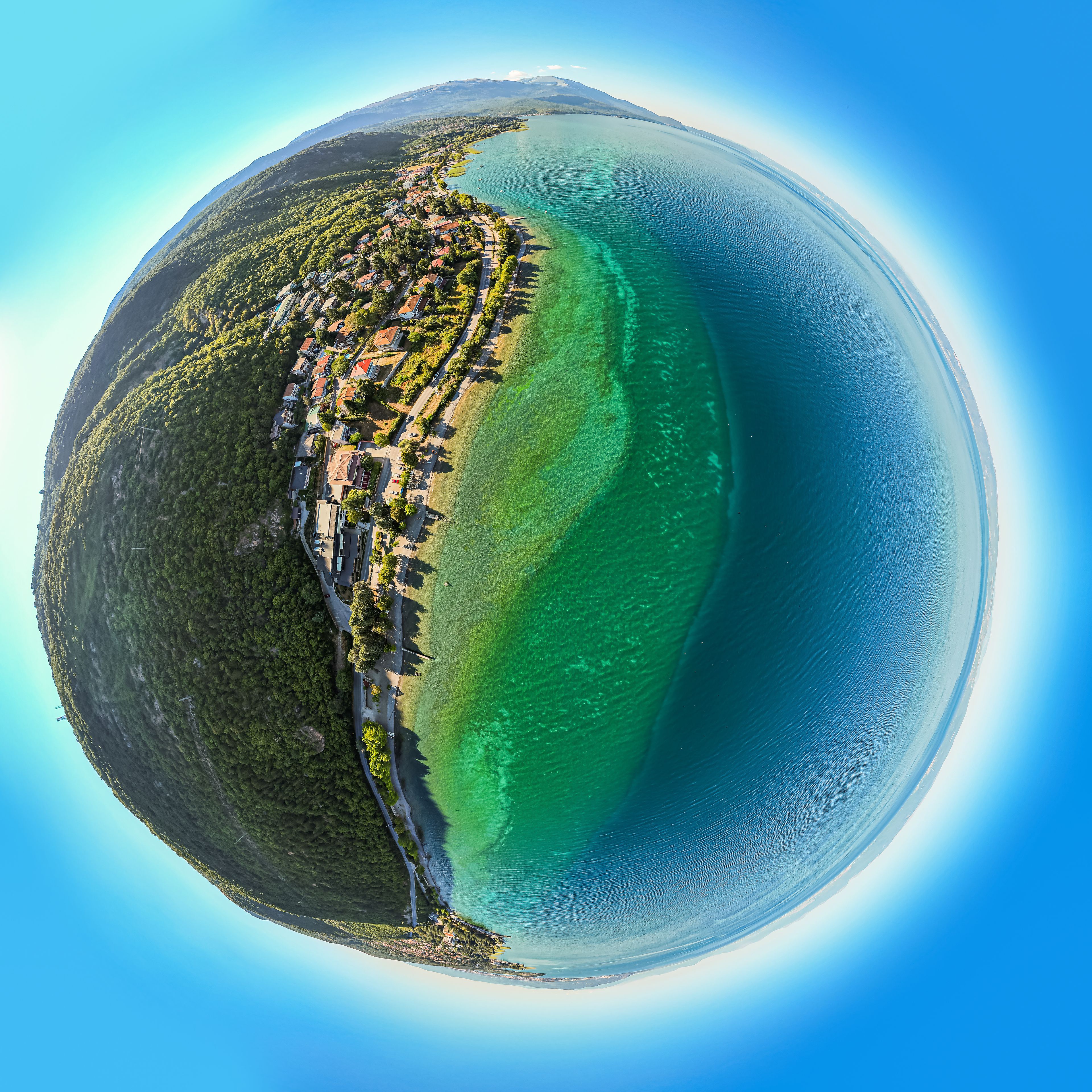 A coastal town with a clear view of the coastline, a road running parallel to the shore, and a mountain in the background.