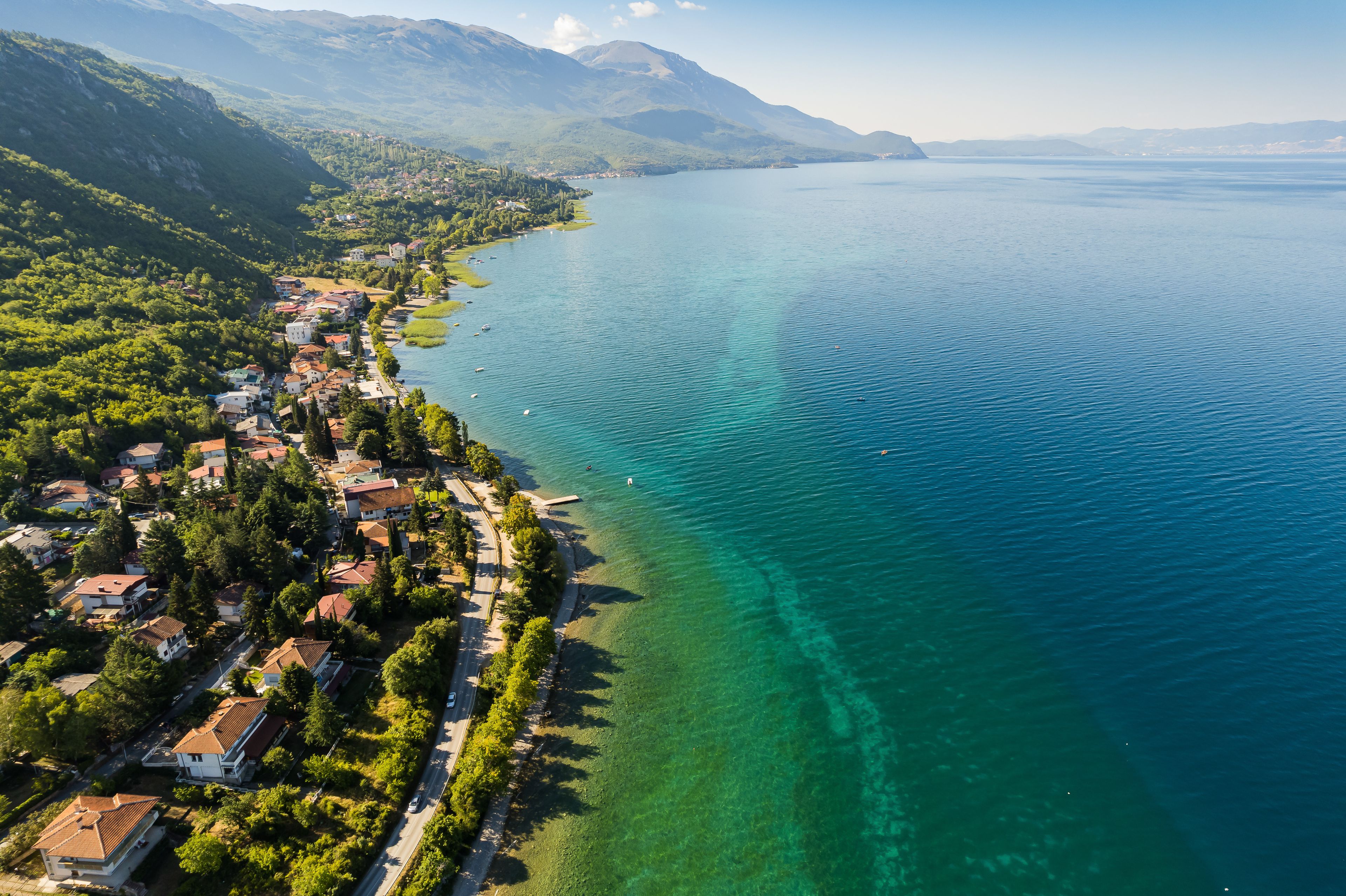 A coastal town with houses along the shoreline, a clear blue lake, and mountains in the background.