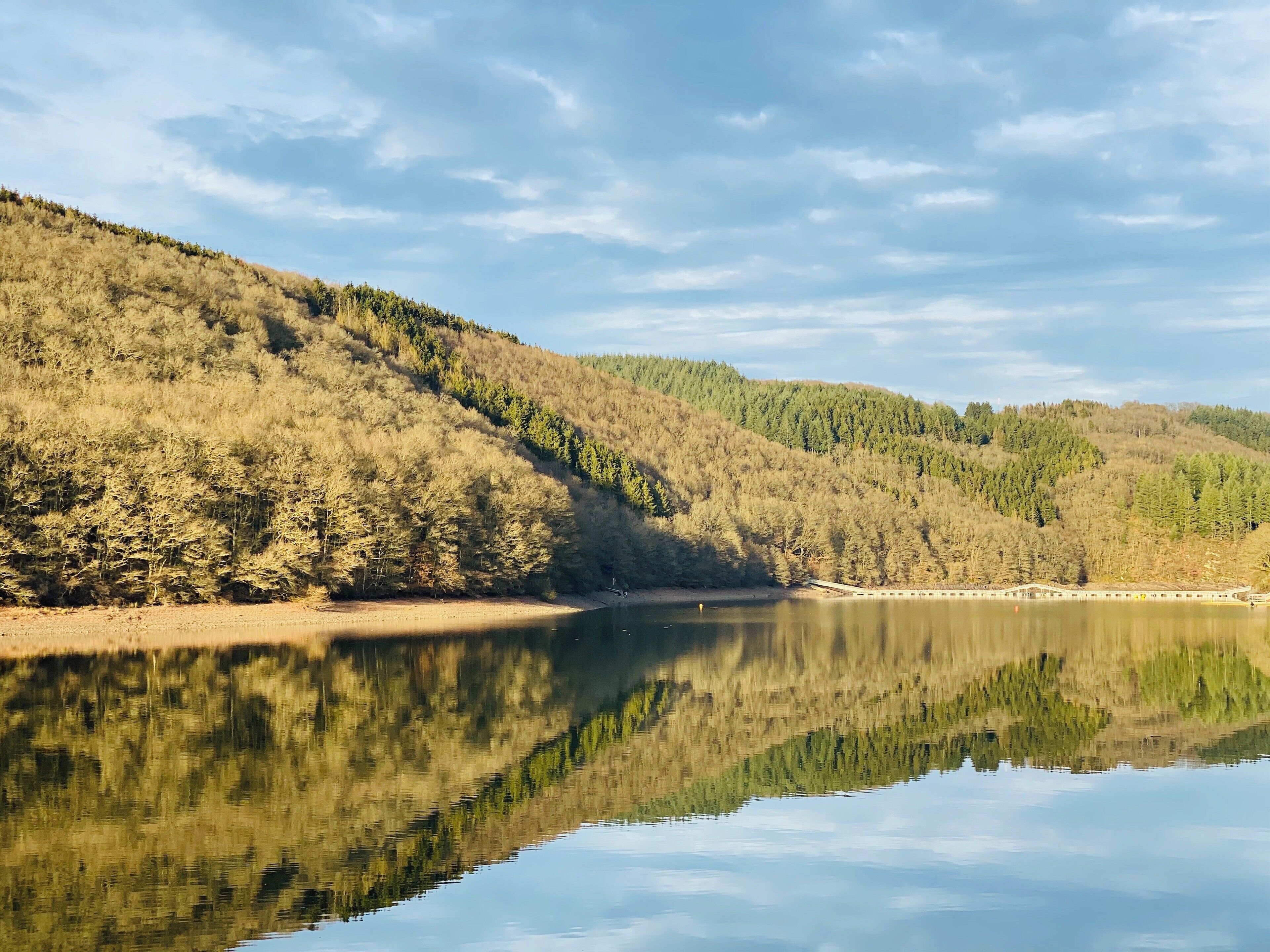 A calm lake reflecting the surrounding hills and sparse trees.