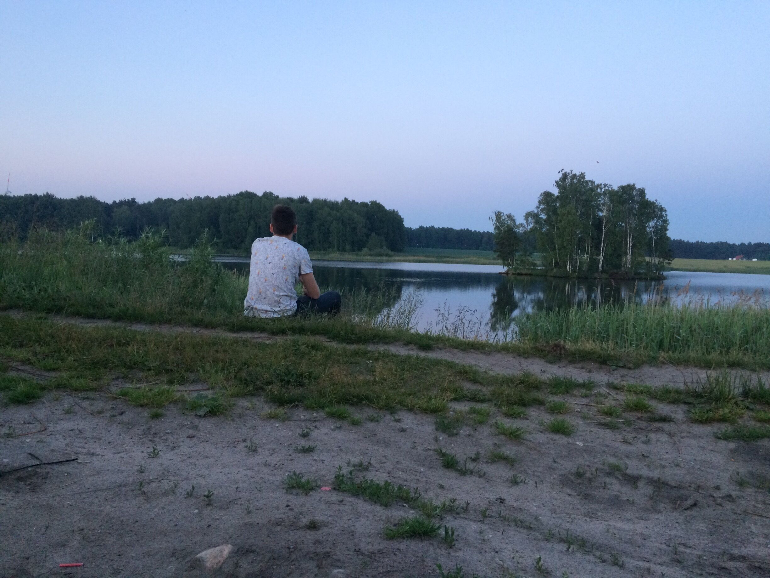 A person sitting by a lake with trees in the background.