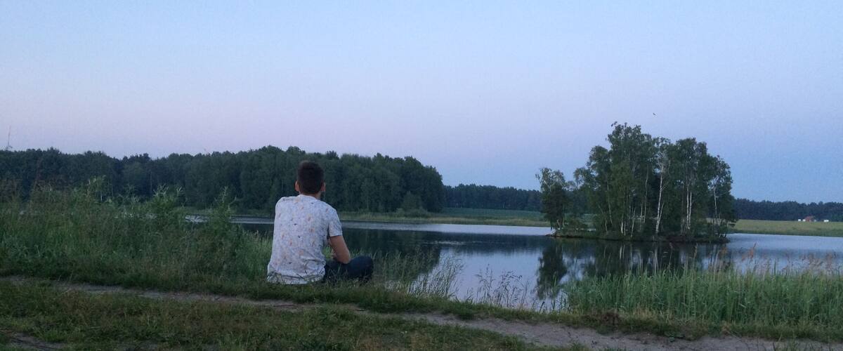 A person sitting by a lake with trees in the background.