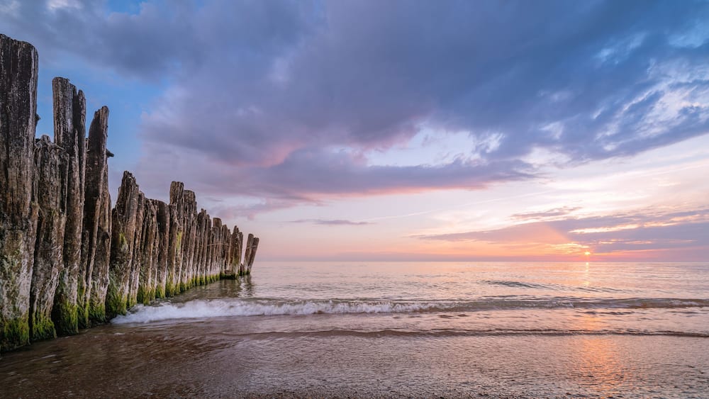 A sunset over a rocky coastline with waves crashing against the shore.