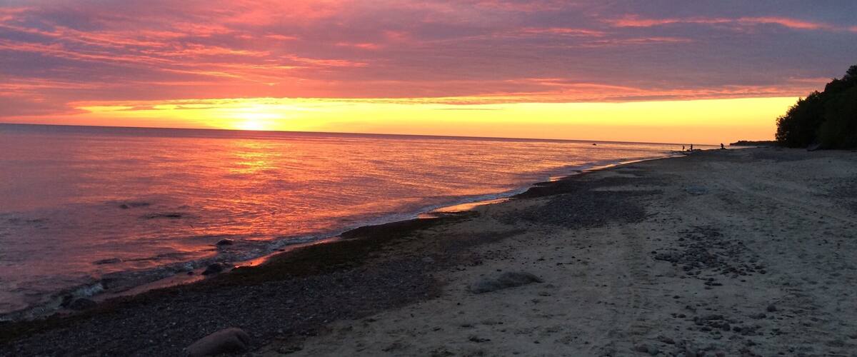 A beach at sunset with a colorful sky and calm sea.