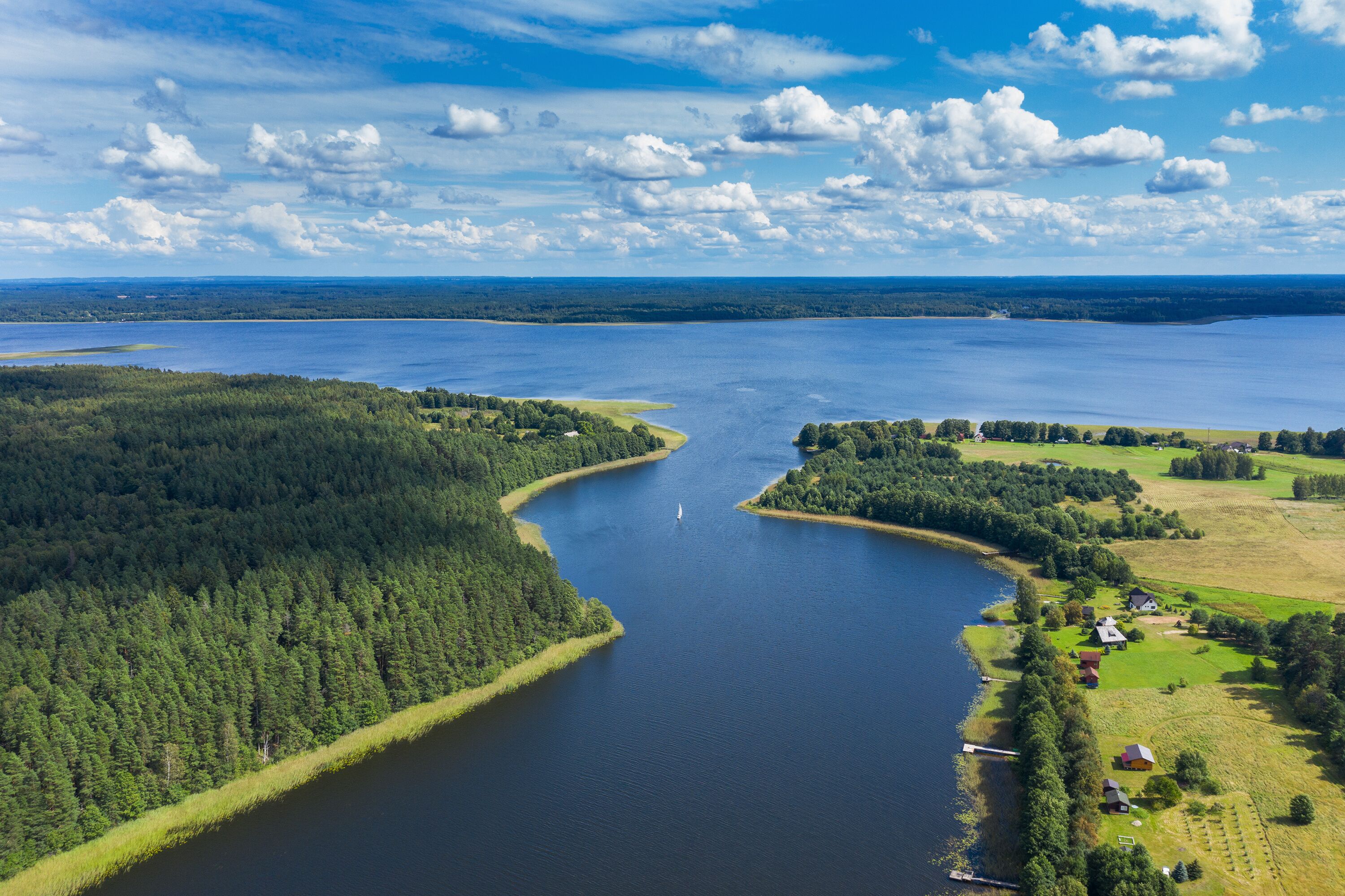 A large lake surrounded by dense forests and a small settlement with houses and a dock.