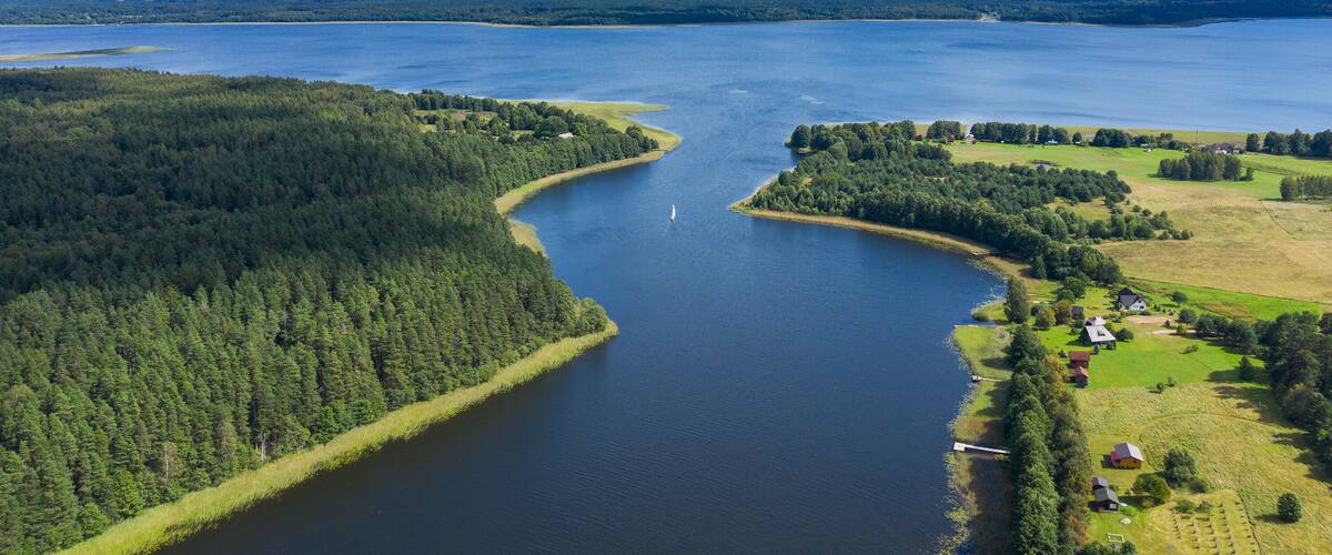 A large lake surrounded by dense forests and a small settlement with houses and a dock.