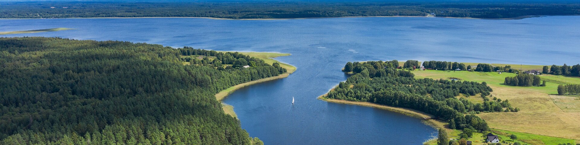 A large lake surrounded by dense forests and a small settlement with houses and a dock.