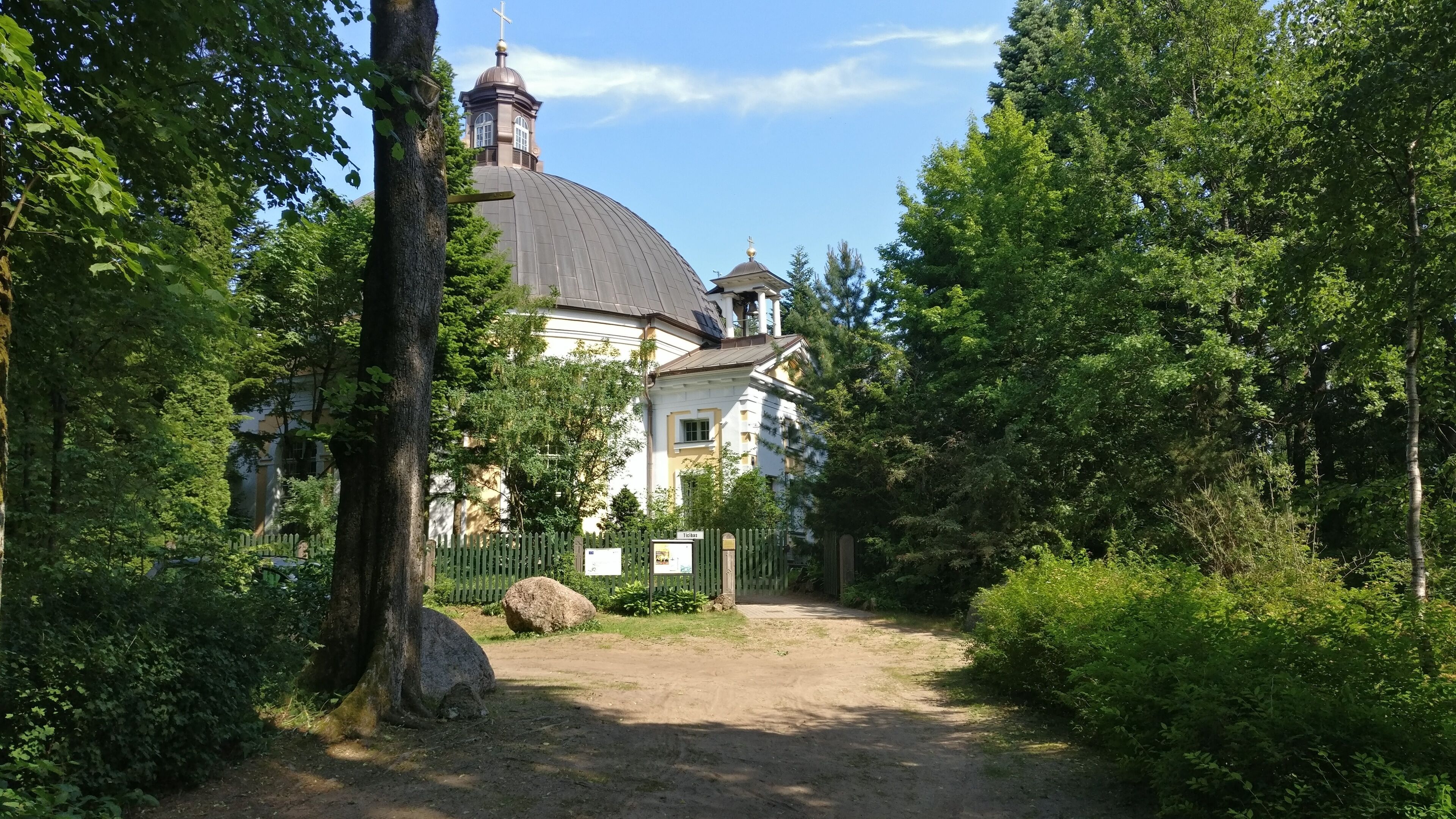 A church with a dome and bell tower surrounded by lush greenery.