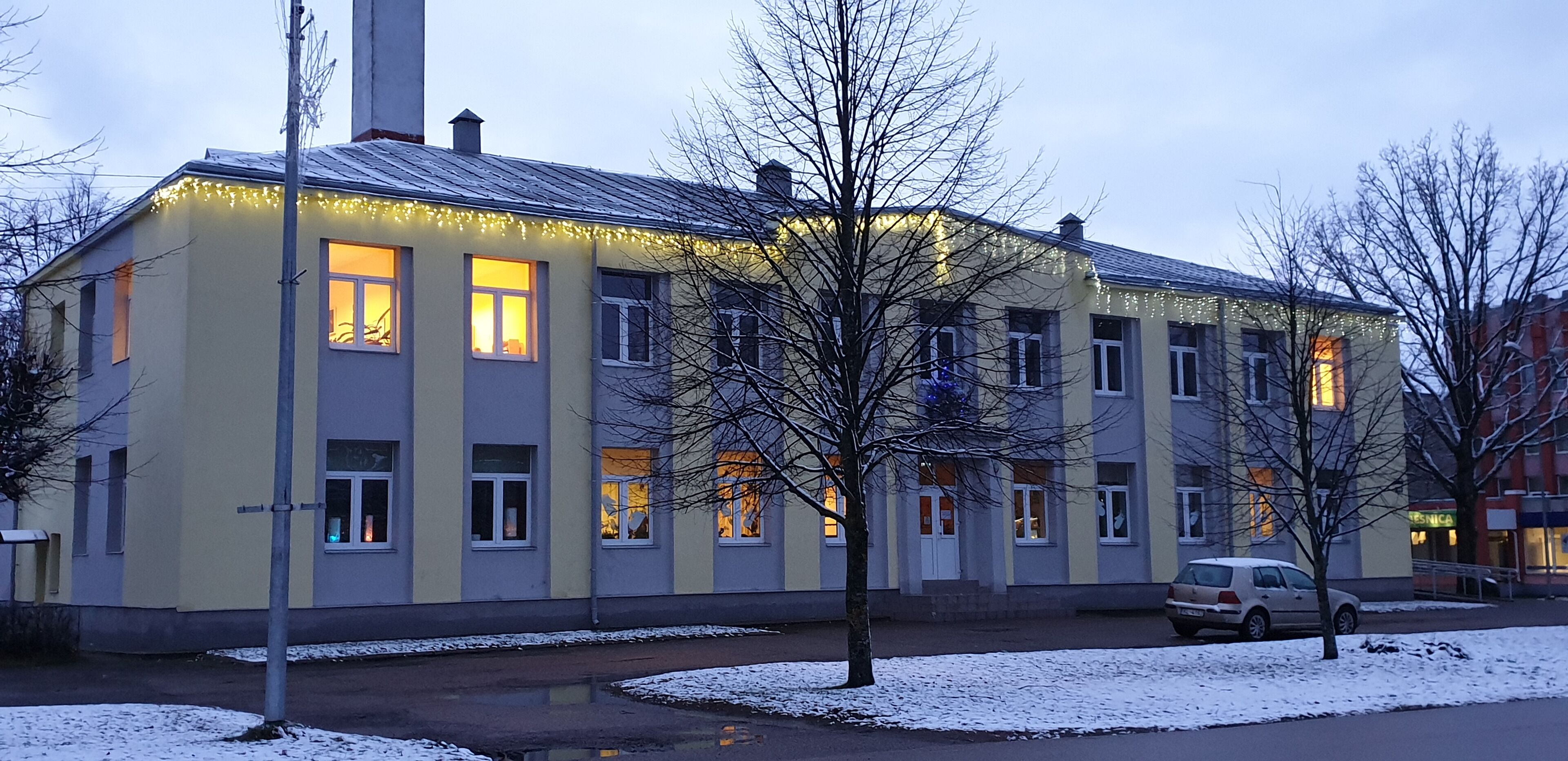 A building with multiple windows, some lit from inside, and a car parked nearby.