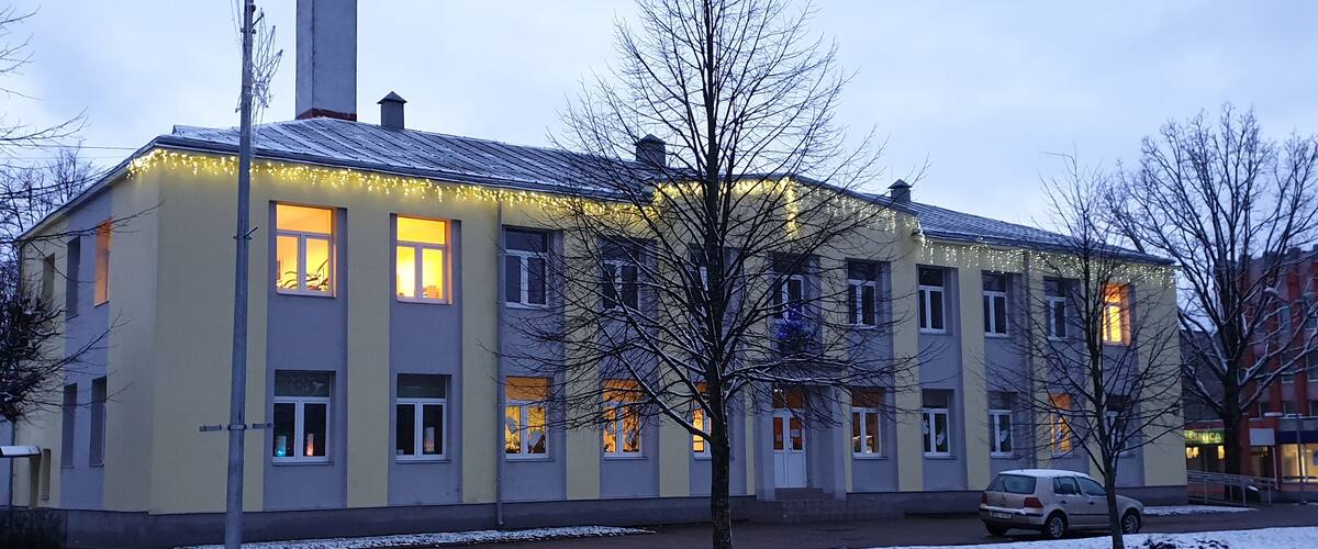A building with multiple windows, some lit from inside, and a car parked nearby.