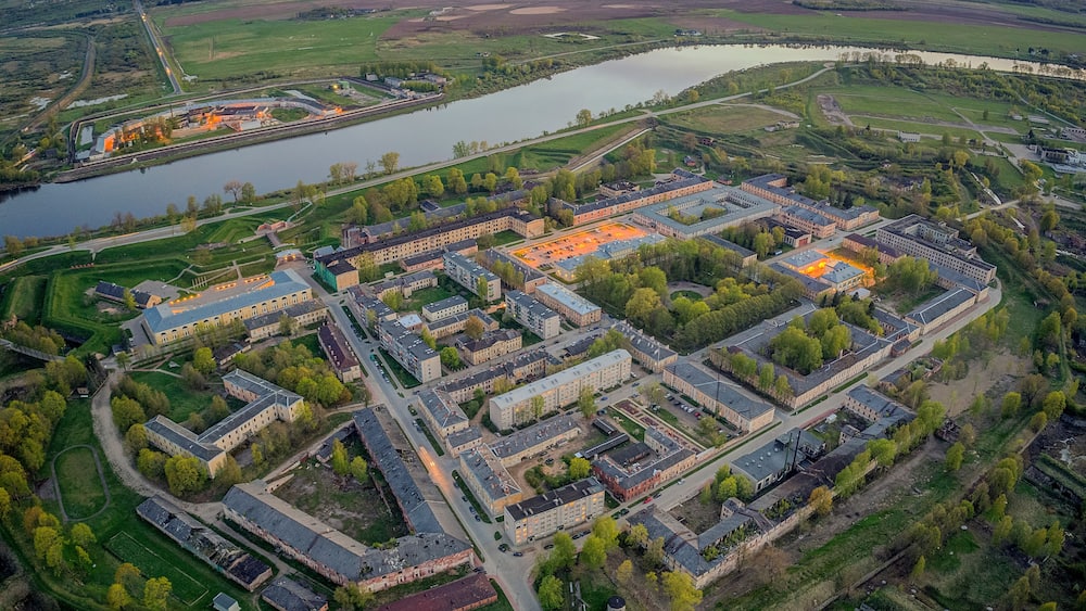 An aerial view of a large campus with multiple buildings, a river, and surrounding green fields.
