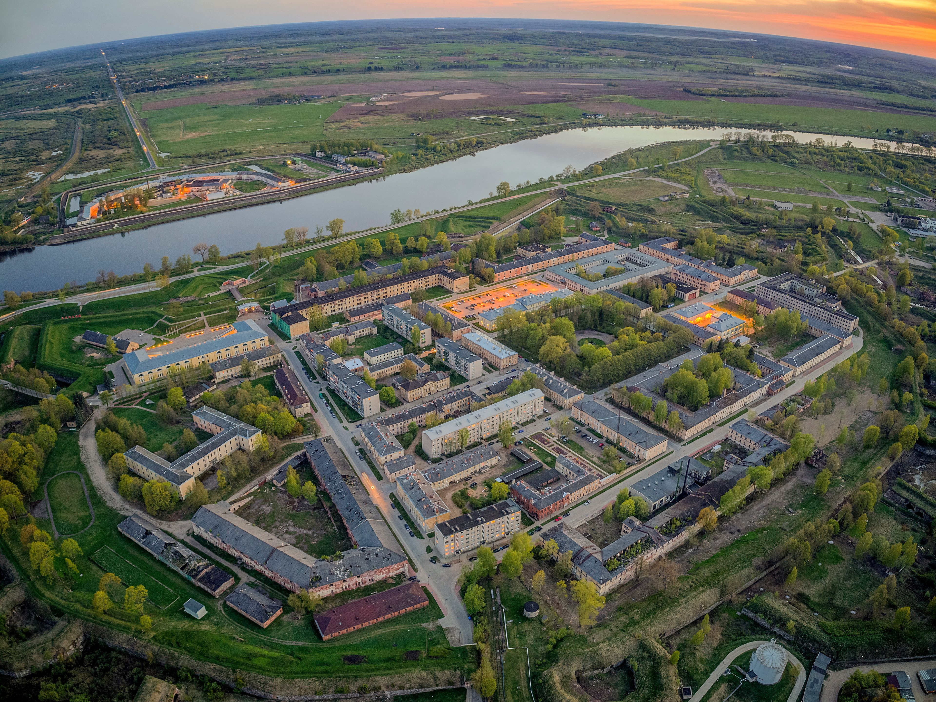 An aerial view of a large campus with multiple buildings, a river, and surrounding green fields.