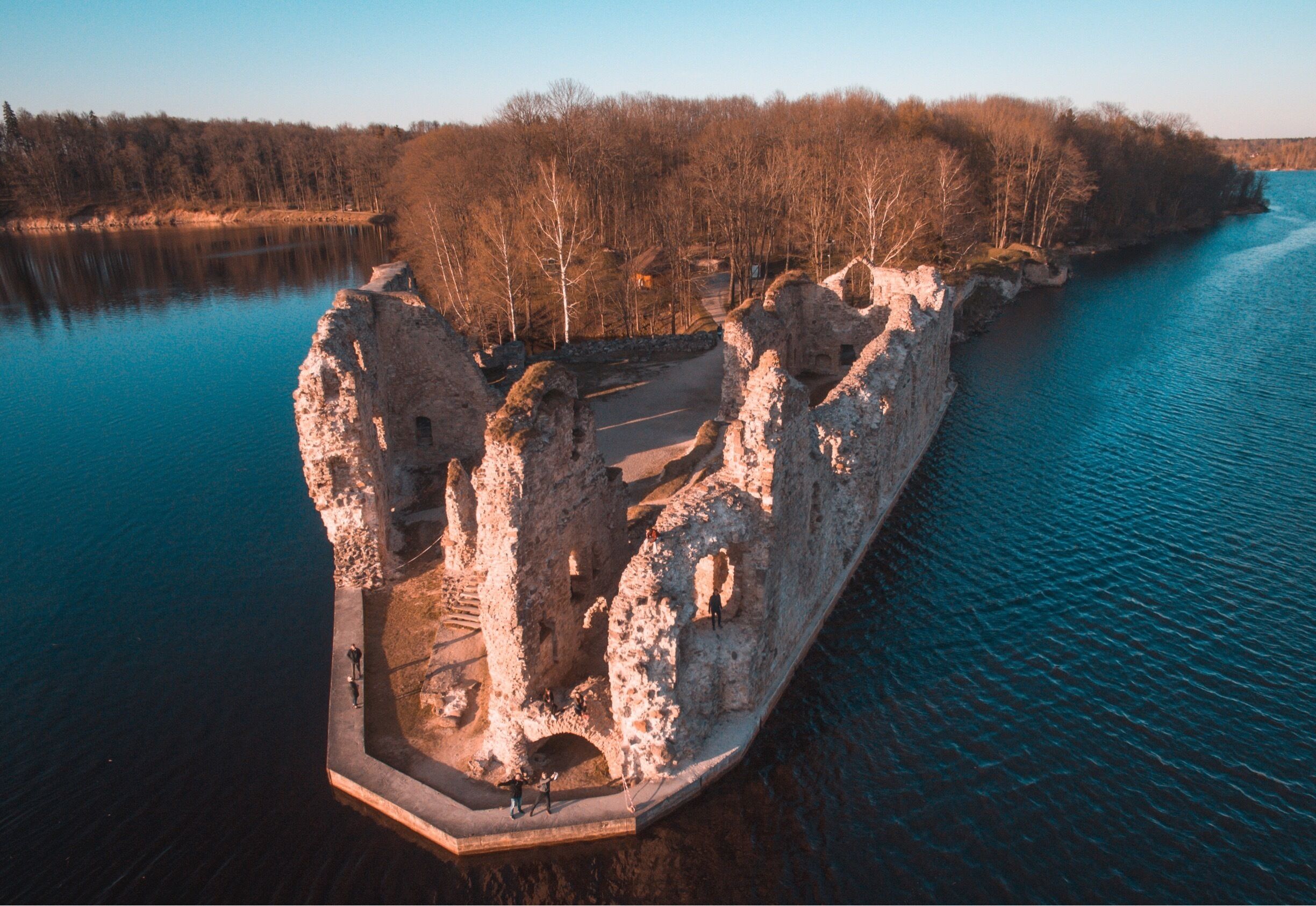An aerial view of a stone ruin with a water body and forested area.