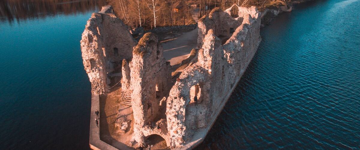 An aerial view of a stone ruin with a water body and forested area.
