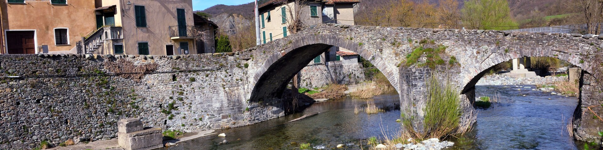 Uma ponte de pedra sobre um riacho límpido, com edifícios de ambos os lados.