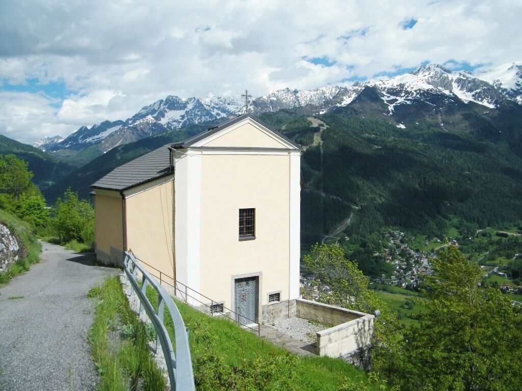 A small building with a sloped roof, surrounded by lush greenery and mountains in the background.