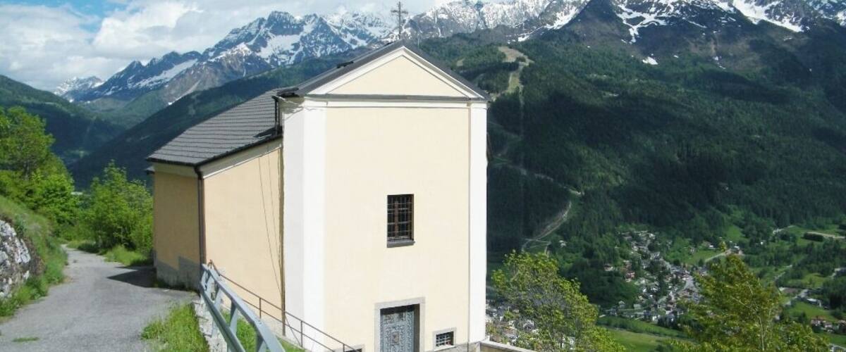 A small building with a sloped roof, surrounded by lush greenery and mountains in the background.