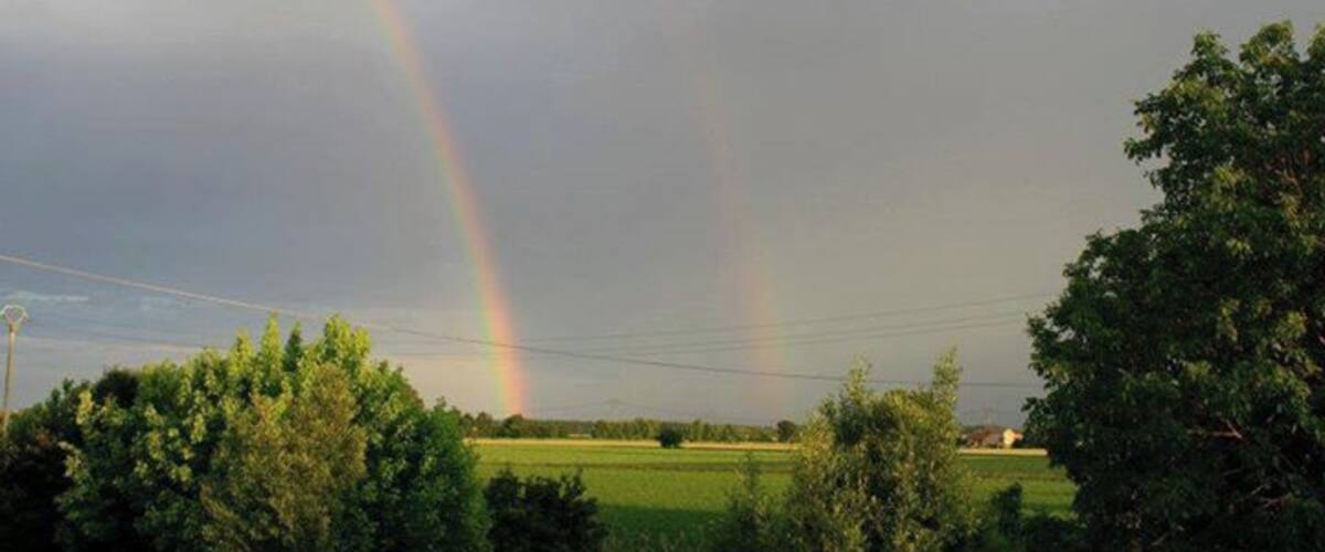 A rural landscape with a double rainbow over a green field.