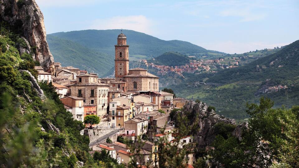 A mountainous village with a prominent church tower, terraced houses, and lush greenery.