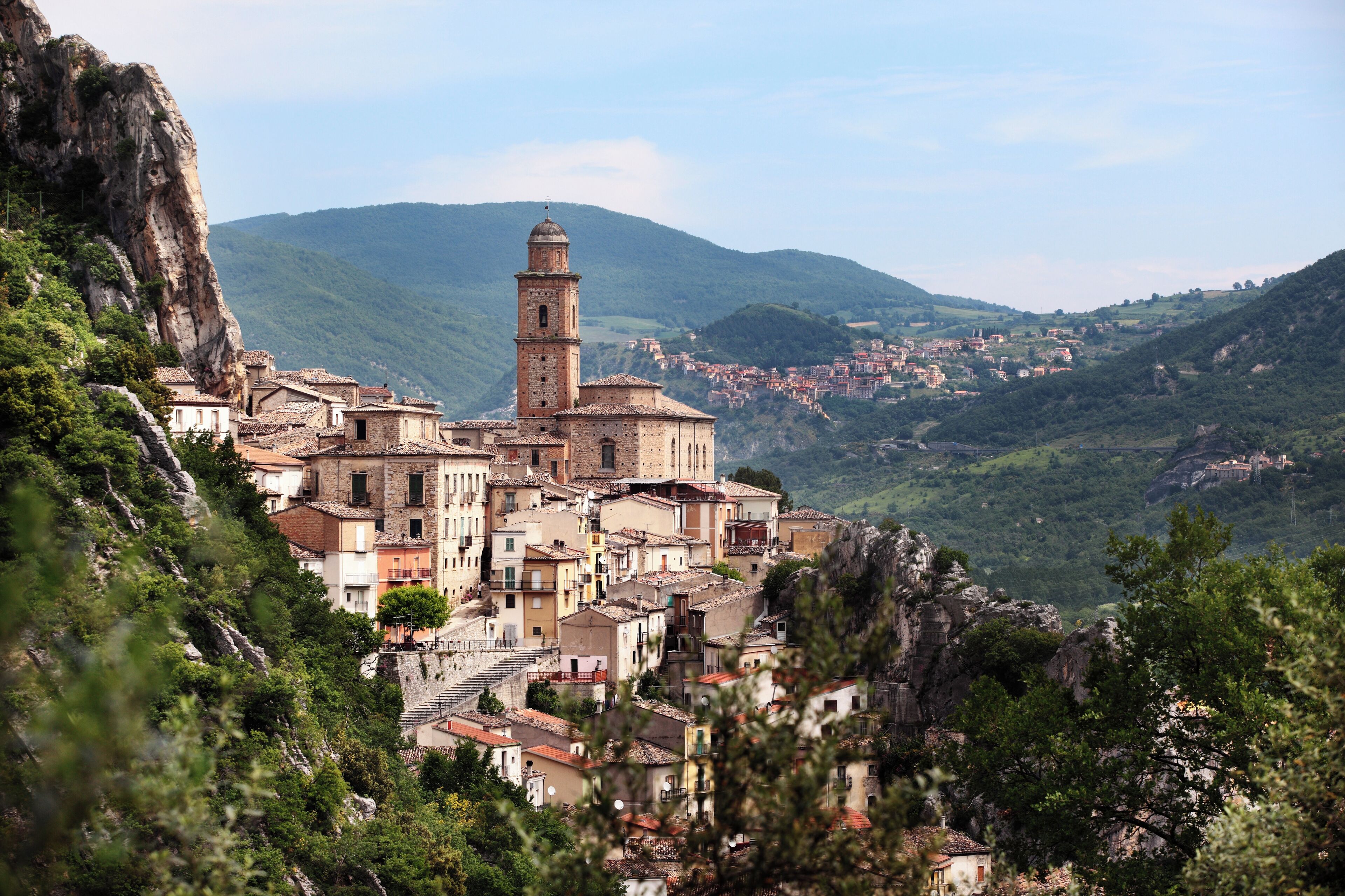 A mountainous village with a prominent church tower, terraced houses, and lush greenery.