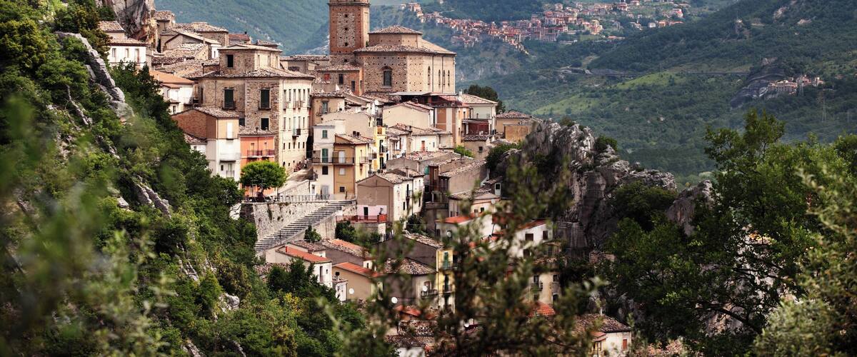 A mountainous village with a prominent church tower, terraced houses, and lush greenery.