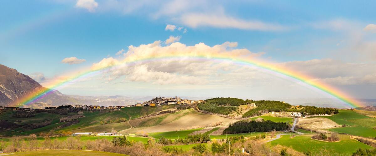 A rainbow over a hilly landscape with a village.