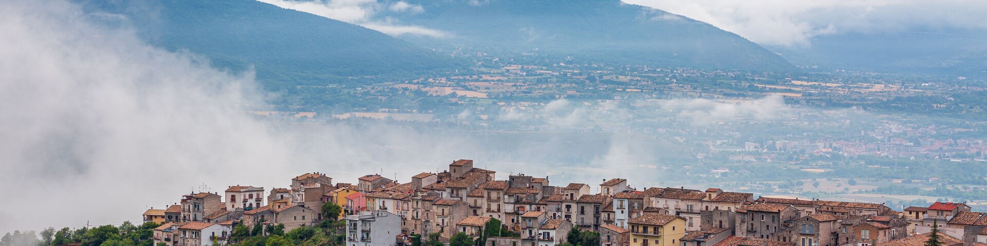Uma vila montanhosa com edifícios em terraços aninhada entre vegetação exuberante e nuvens.