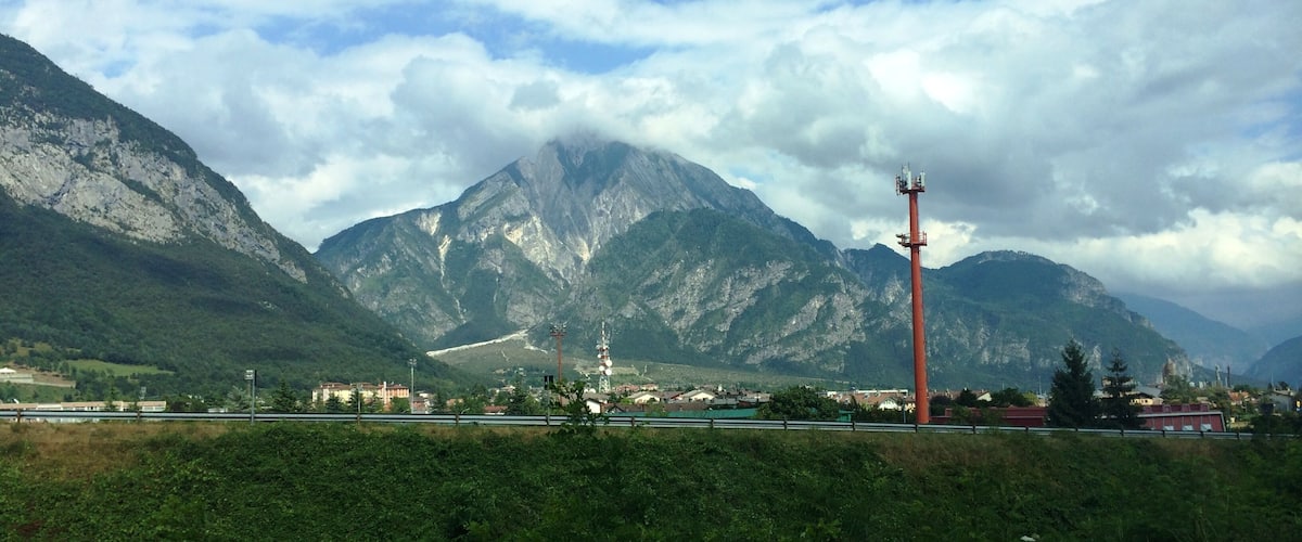 A mountainous landscape with a prominent red communication tower, a river, and a small town with buildings.