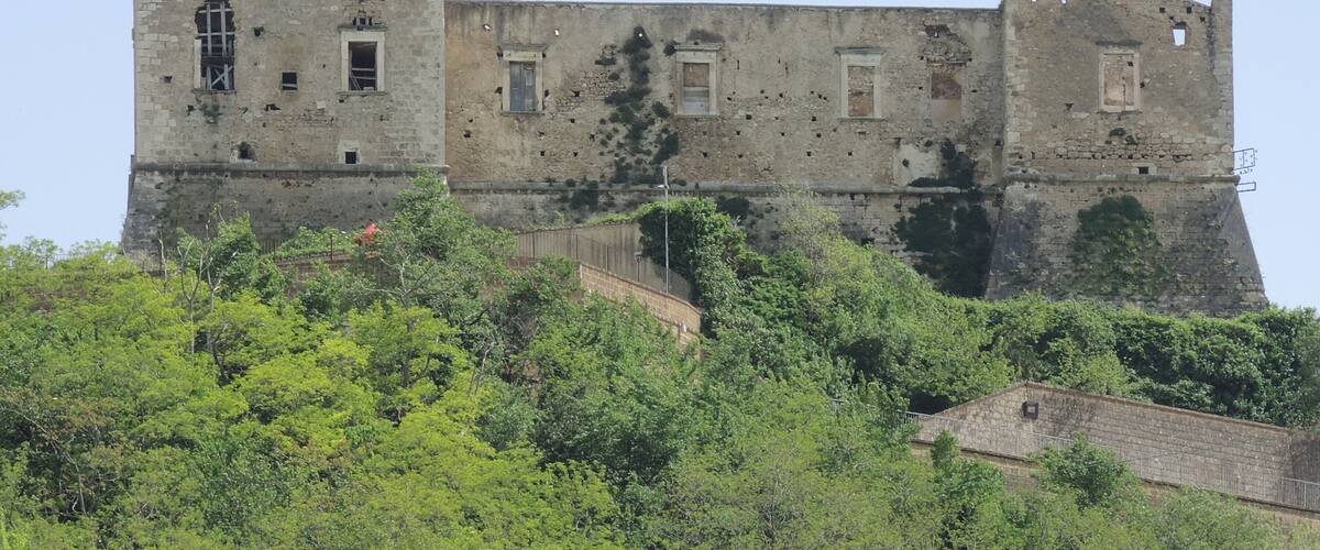 A historic stone castle with battlements, surrounded by lush greenery.