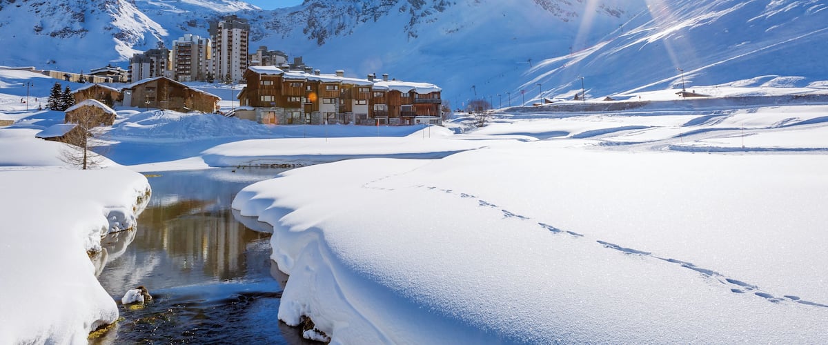 A snow-covered landscape with a mountain, a river, and buildings in the background.