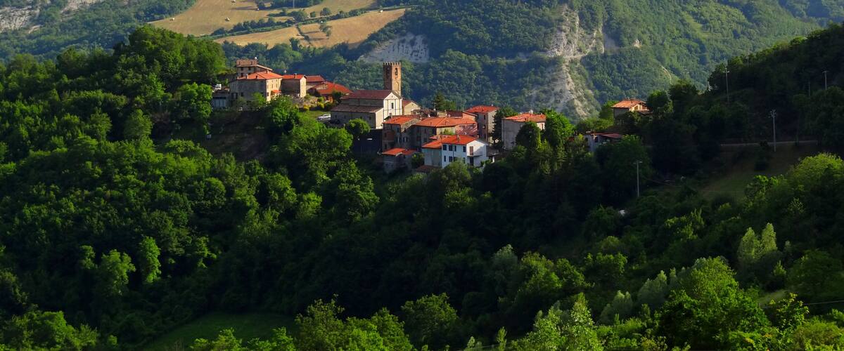 A village nestled in a valley surrounded by lush green hills and a prominent church tower.