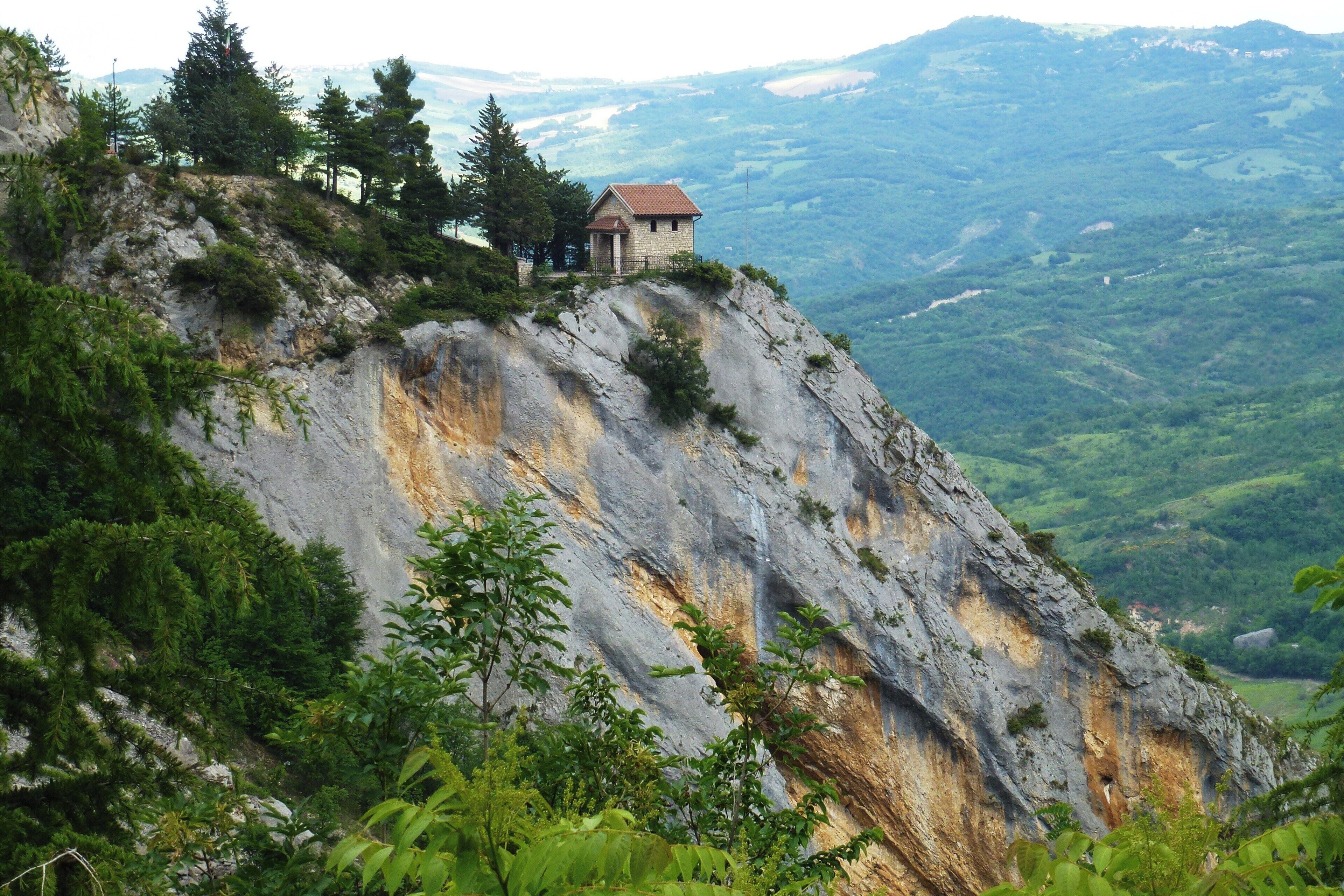 A small stone building on a rocky hillside with a view of a valley below.