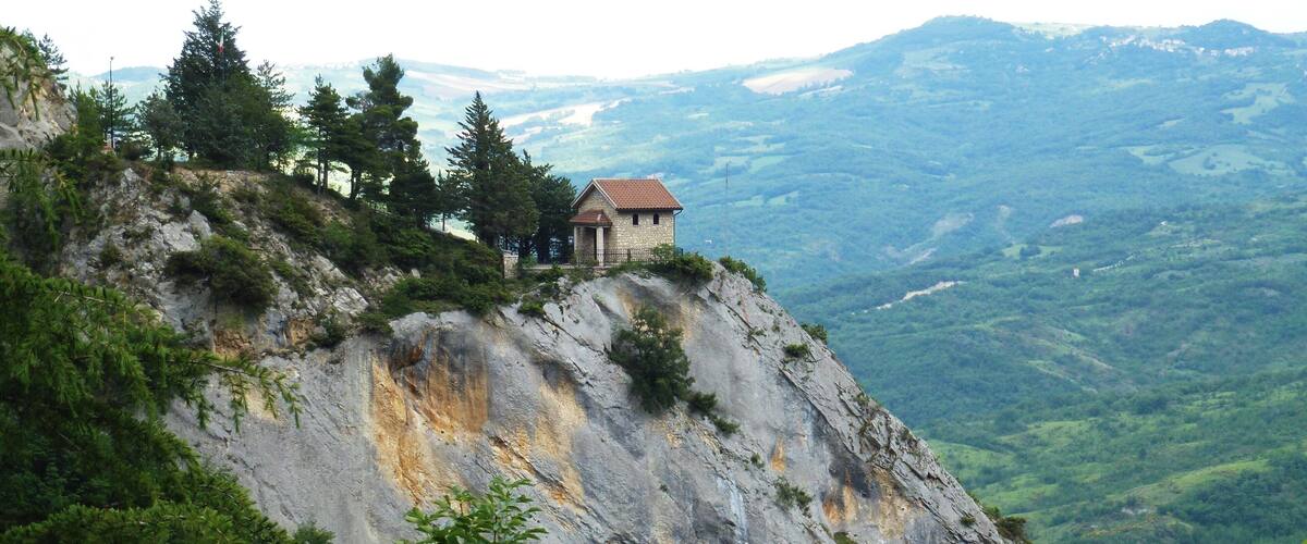A small stone building on a rocky hillside with a view of a valley below.
