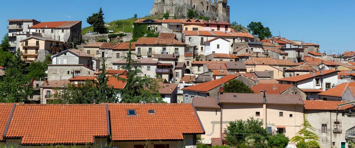 A town with red-tiled roofs and a historic stone castle on a hill.