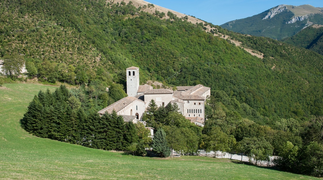 A historic stone building with a bell tower, surrounded by lush green hills and a clear blue sky.