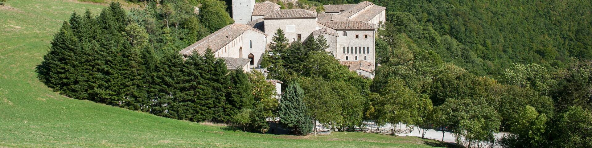 A historic stone building with a bell tower, surrounded by lush green hills and a clear blue sky.