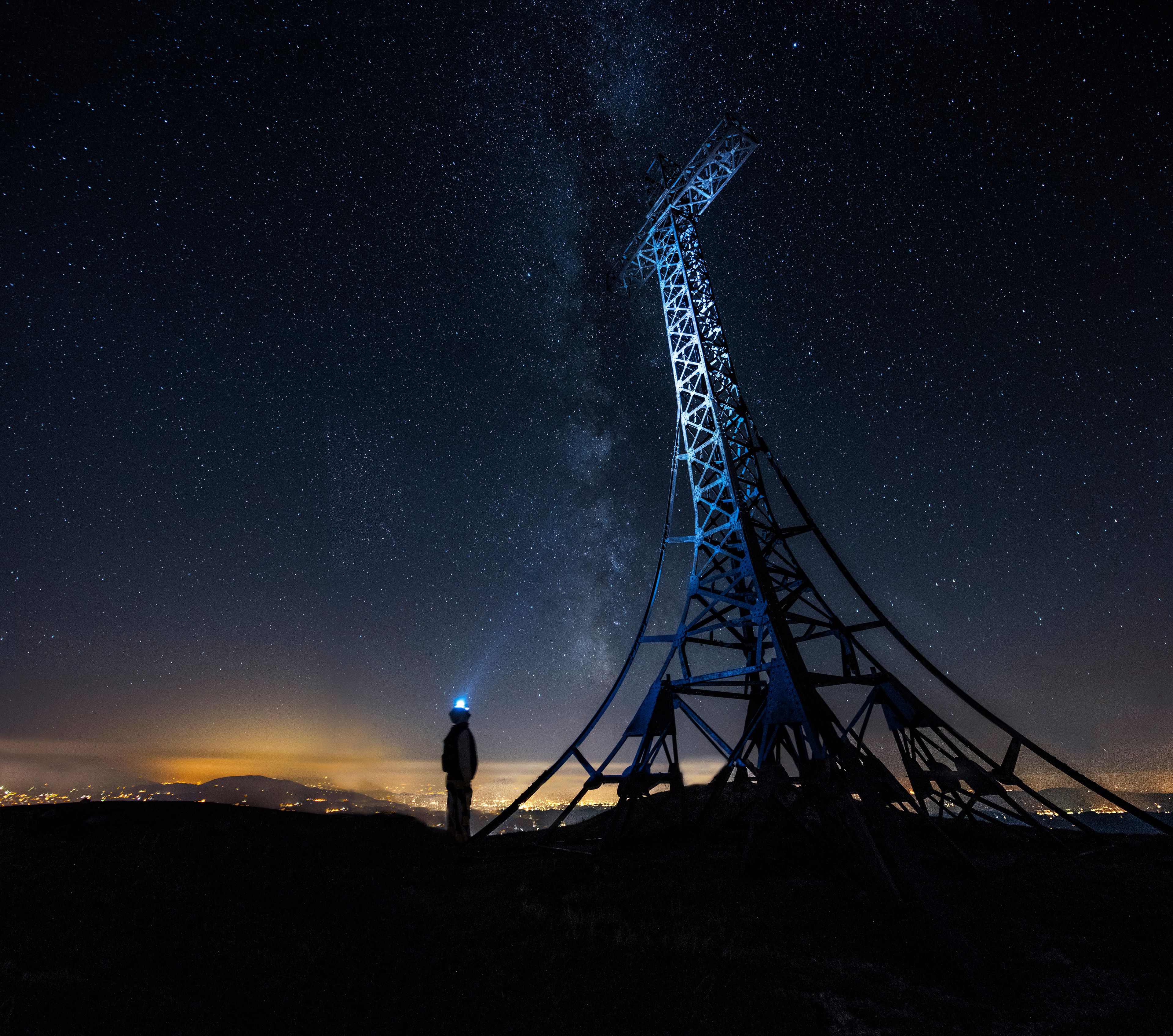A person standing near a tall, illuminated electrical tower against a starry night sky.