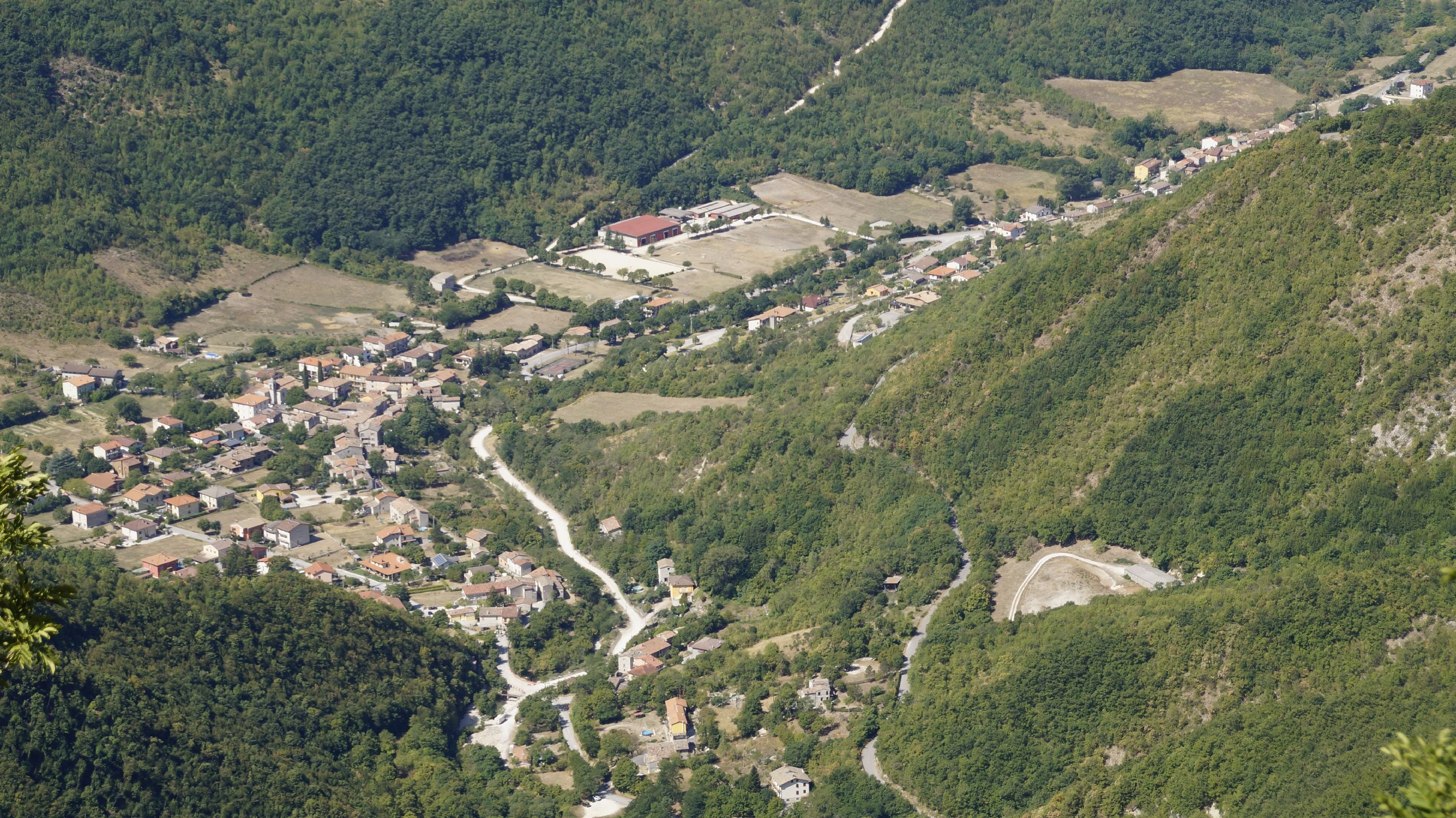 A mountainous village with a winding road, dense forests, and scattered houses.