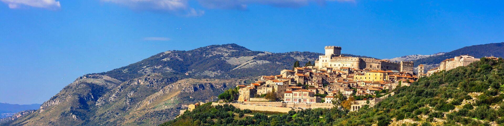 Un pueblo histórico en una ladera, con una torre destacada, rodeado de montañas y vegetación exuberante.