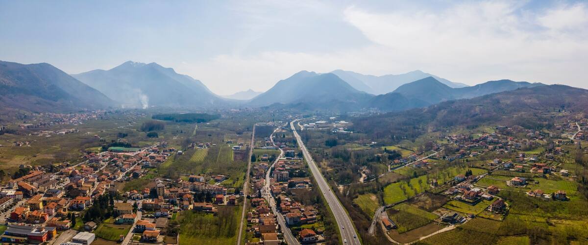 An aerial view of a town nestled between mountains, with a prominent road running through the center.